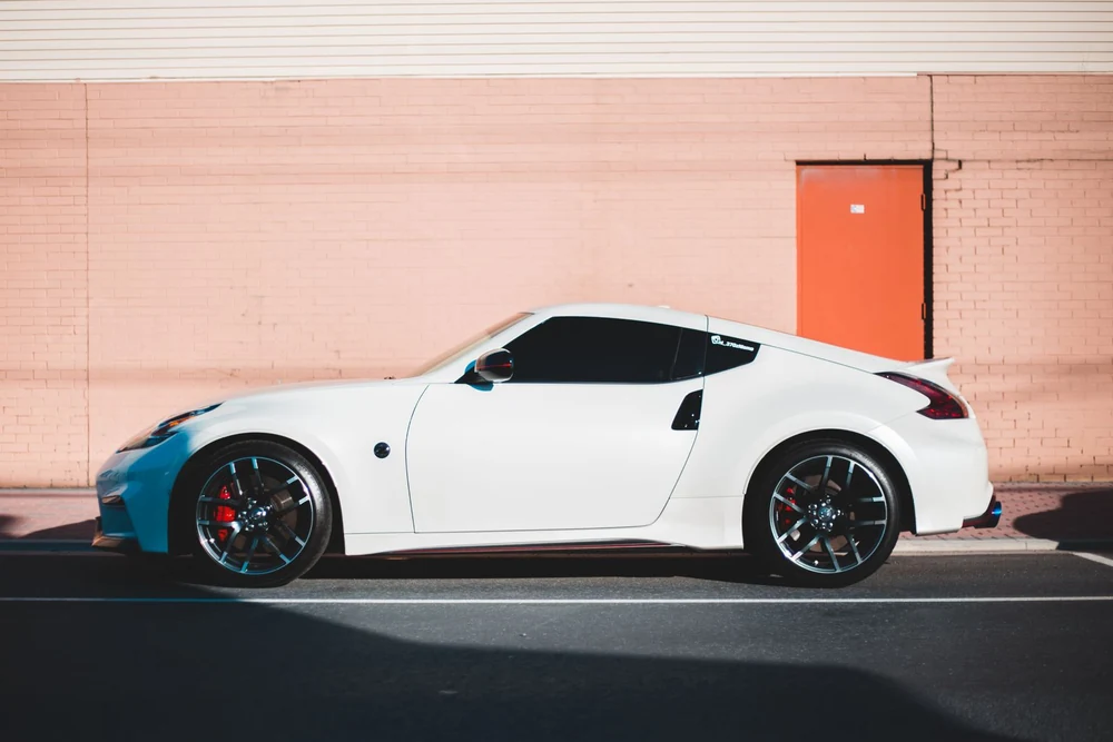 A white coupe parked in front of a sunlit peach brick wall.